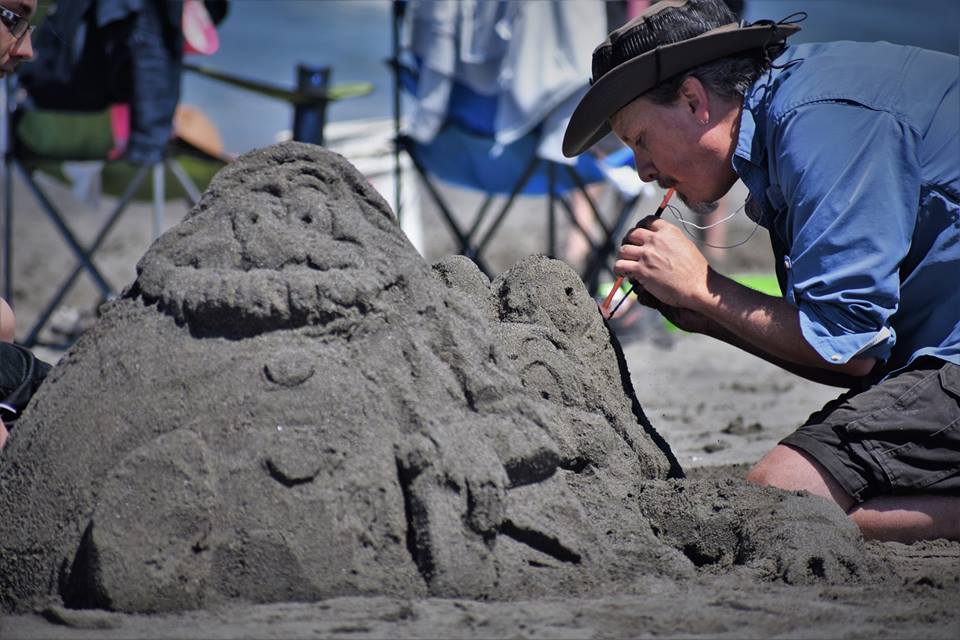 Using a straw to blow away sand while details are carved. Photo courtesy of Friends of the Dunes.